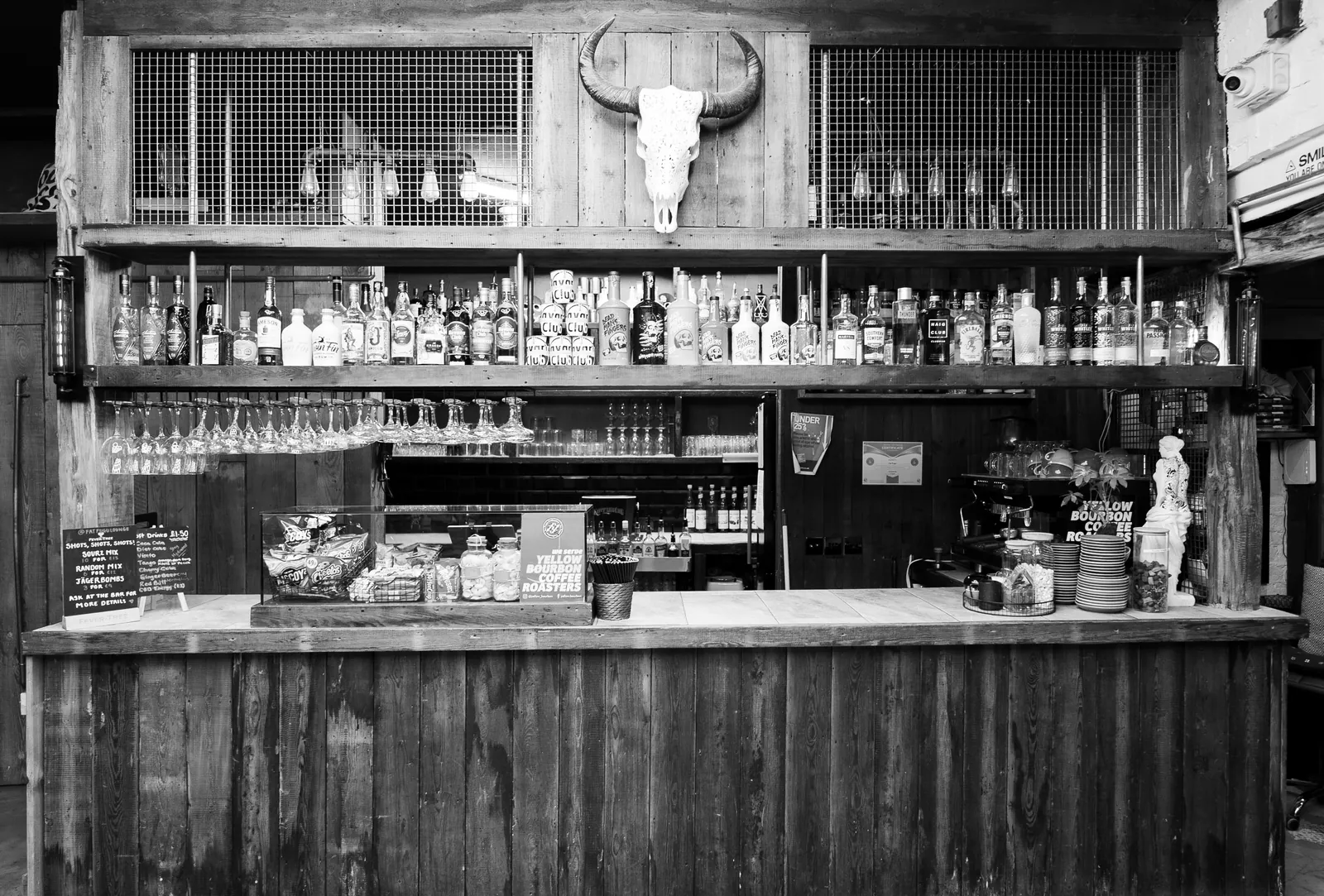 The cocktail bar: a long reclaimed-timber counter under a lit back-bar of bottles and glassware, a longhorn skull mounted above the shelves.