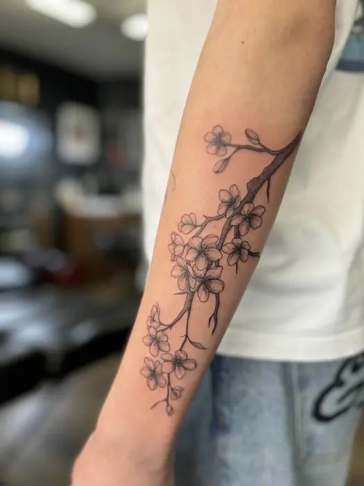 A fine line blossom branch running the length of the forearm, delicate and widely spaced.
