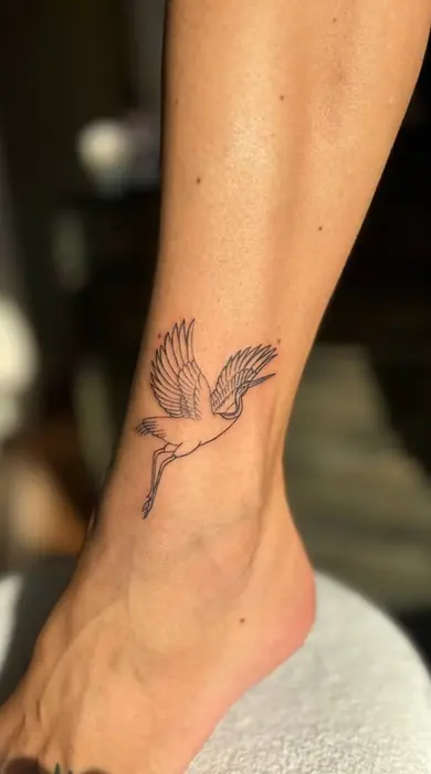 A fine line crane in flight on the ankle, wings extended, worked in a single delicate line weight.