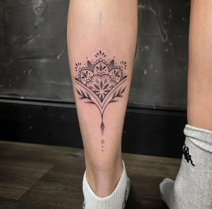 A fine line ornamental piece down the shin: a small mandala with fine dropped linework beneath it.
