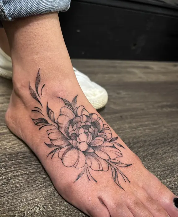 A fine line peony across the top of the foot, single-weight linework with minimal shading.