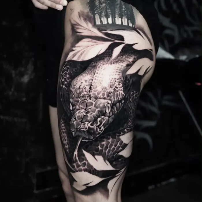 A black and grey thigh piece: koi and foliage worked around a skull, photographed against a brick wall.