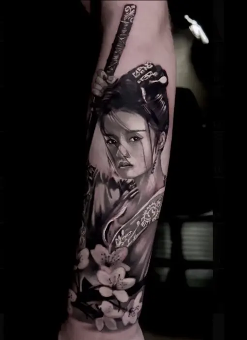 A black and grey Japanese sleeve: a geisha in profile worked among blossom and cloud, running the length of the forearm.