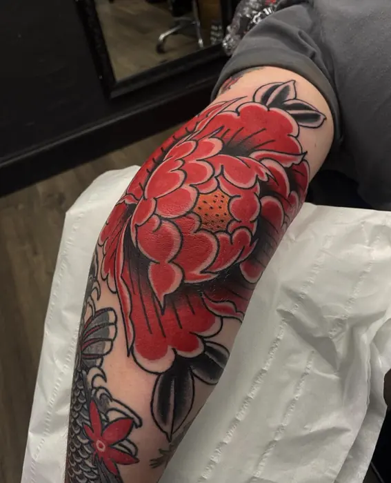 A Japanese forearm and upper-arm piece, a large red peony opening over black and grey wind bars.