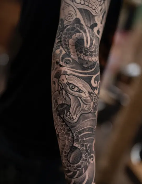 A black and grey Japanese sleeve running wrist to elbow: a snake coiled through ornamental scroll and a skull.