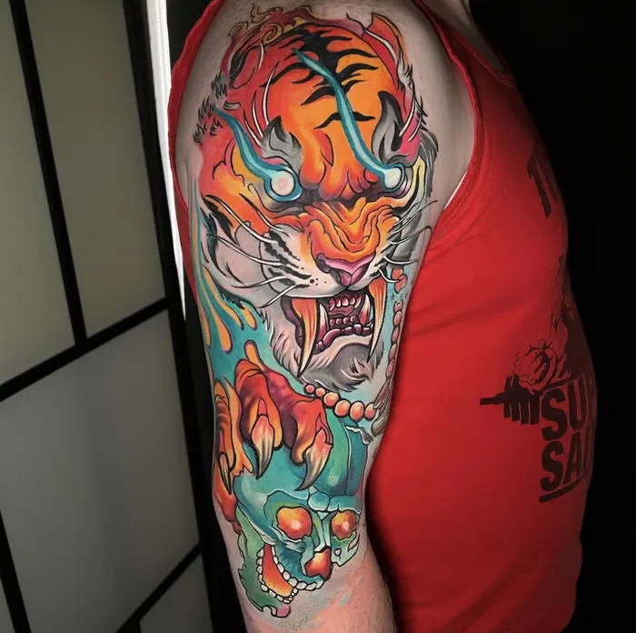 A Japanese upper-arm sleeve in full colour: a snarling tiger among stylised flame and wave, greens and oranges over a black background field.