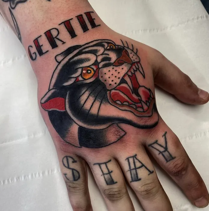 A neo-traditional panther head on the back of the hand in bold black and red, lettering across the fingers.