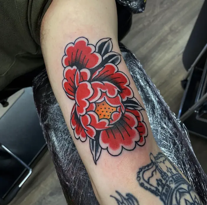 A neo-traditional red peony on the forearm, bold outline and flat colour packing.