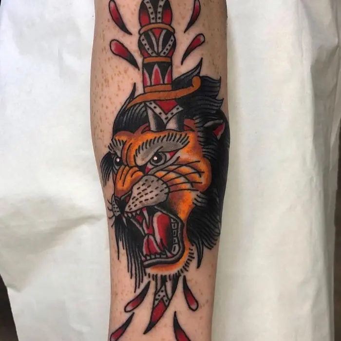 A neo-traditional roaring tiger head impaled on a dagger, forearm, orange and black.