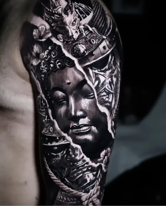 A black and grey realism arm piece: a serene stone Buddha face set into ornamental and architectural detail.
