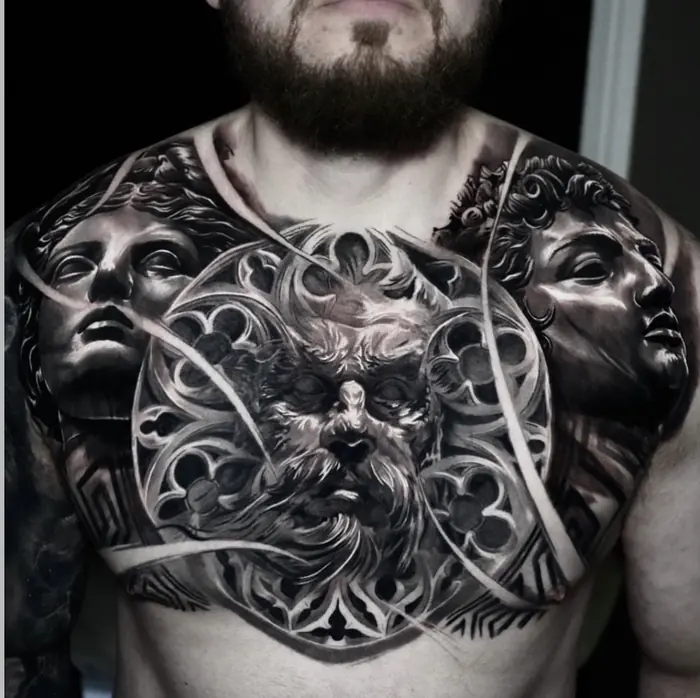 A black and grey realism chest panel: classical statuary and ornamental scroll worked across both pectorals and up to the collarbones.