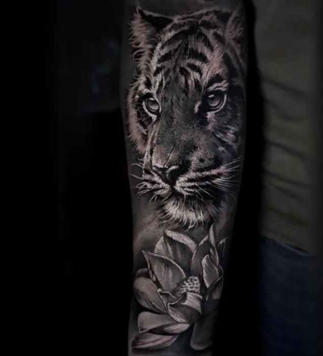 A black and grey realism tiger on the forearm, lotus and foliage worked in beneath it.